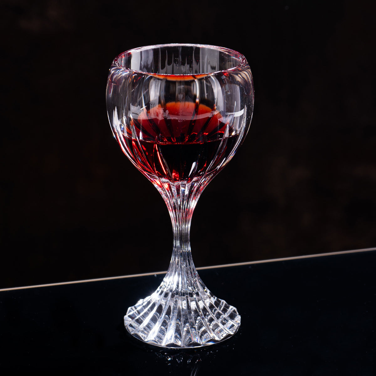 Classic cut stemmed glass with red beverage in dark background setting