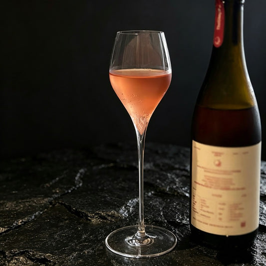 Elegant stemmed glass with wine bottle and beverage on dark table surface