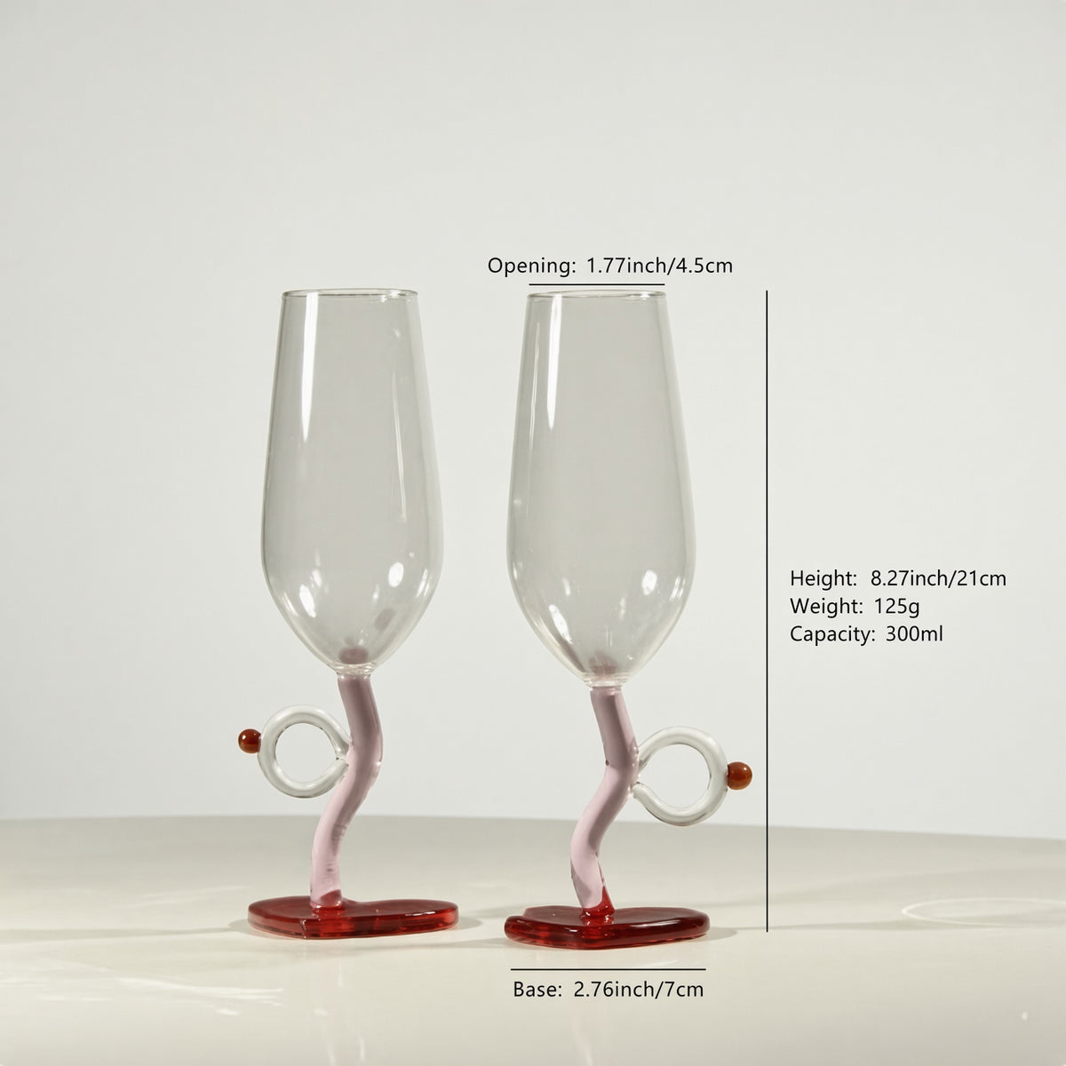 Two clear glass champagne flutes with twisted pink stems and red bases, shown on a light gray background with measurement text and lines indicating dimensions.